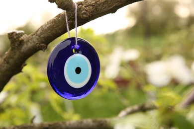 Photo of Evil eye amulet hanging on blossoming spring tree outdoors, closeup. Space for text