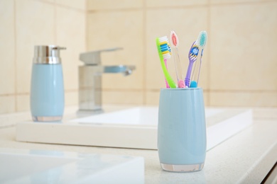 Photo of Cup with different toothbrushes near sink in bathroom. Dental care