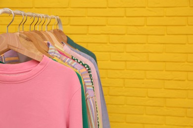 Rack with stylish clothes near yellow brick wall, space for text