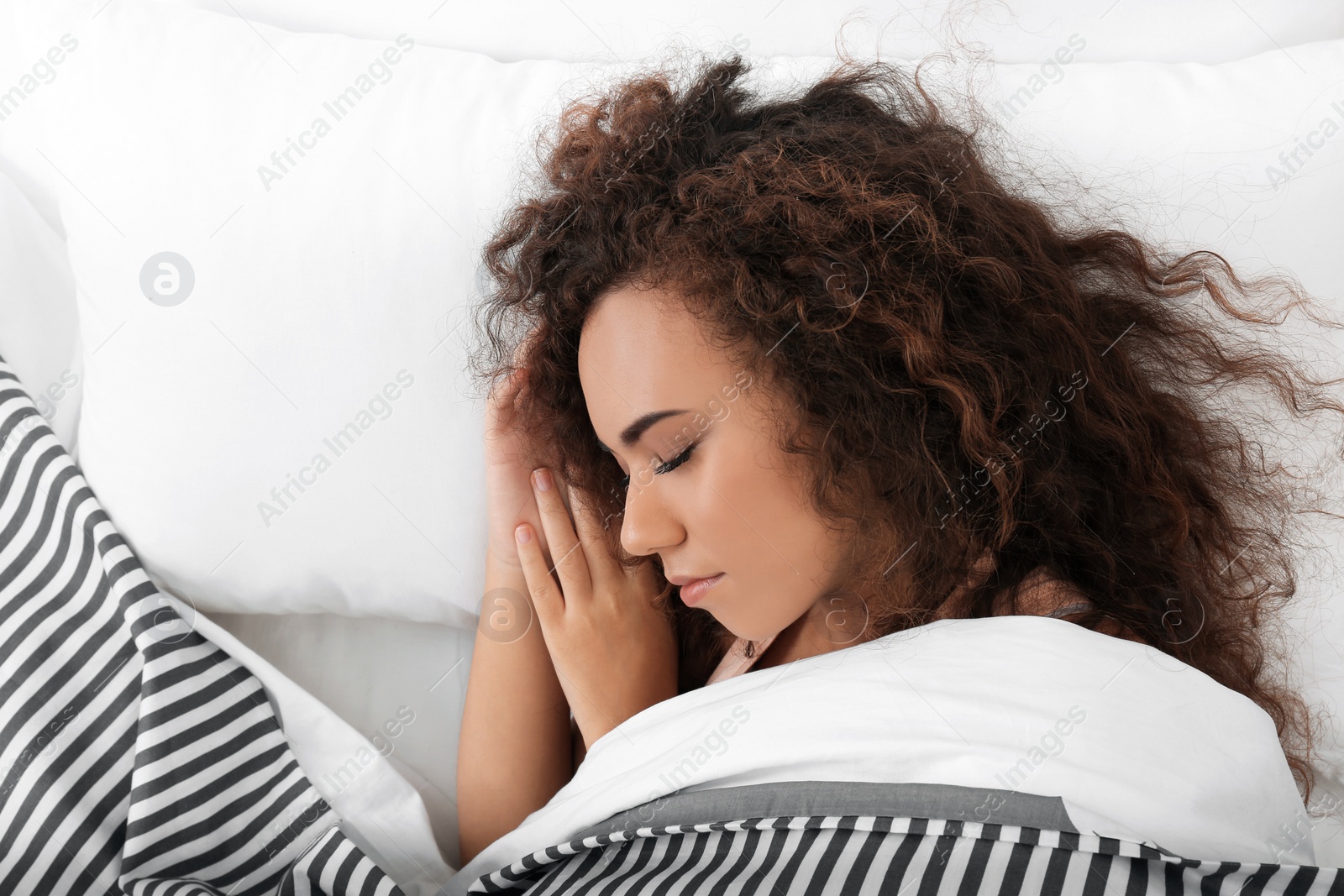 Photo of Young African-American woman sleeping on soft pillow, top view. Bedtime