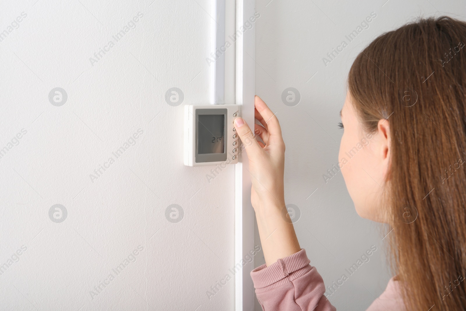 Photo of Woman adjusting thermostat on white wall. Heating system