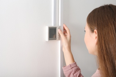 Woman adjusting thermostat on white wall. Heating system