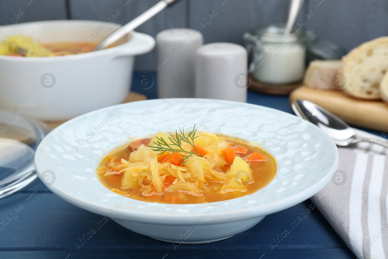 Photo of Delicious sauerkraut soup with carrot and dill on blue wooden table