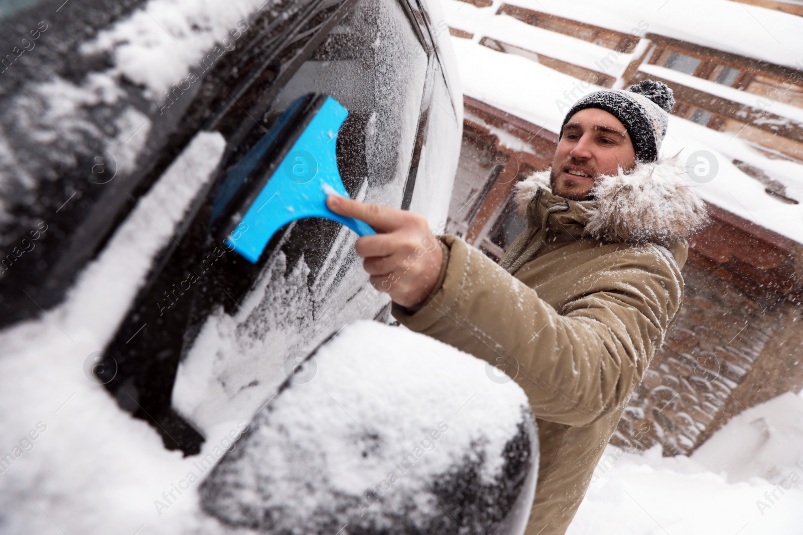 Photo of Young man cleaning snow from car window outdoors on winter day