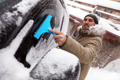 Young man cleaning snow from car window outdoors on winter day