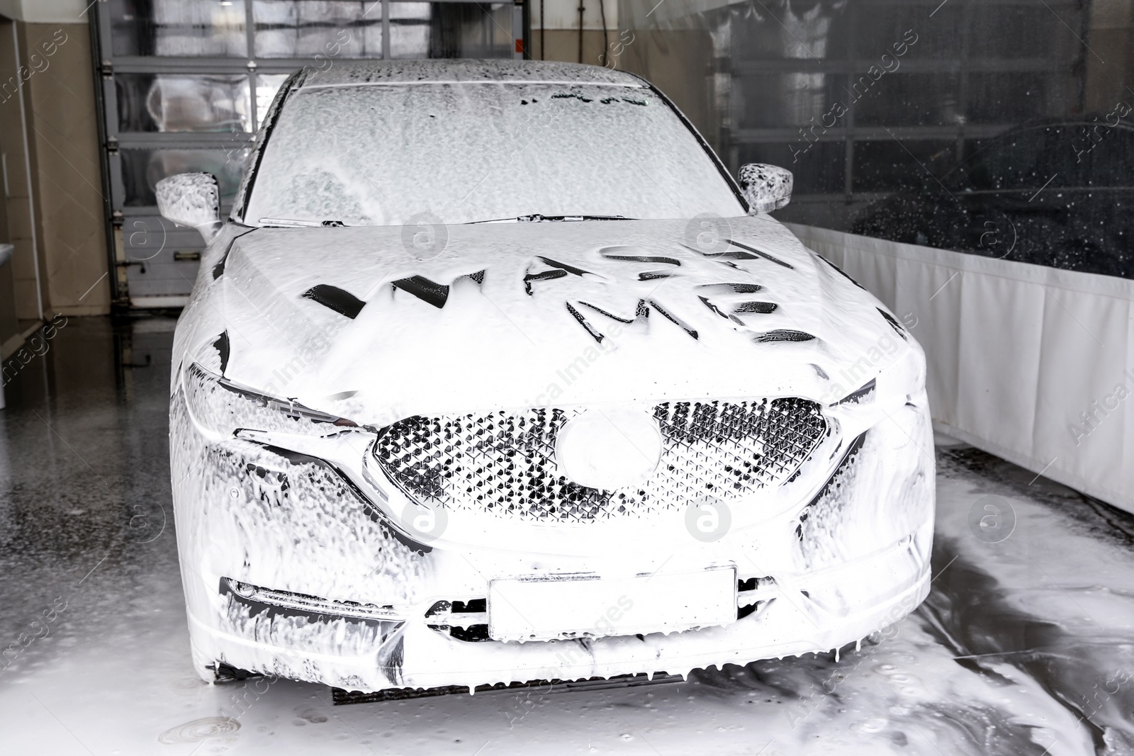 Photo of Inscription WASH ME on automobile covered with foam at car wash