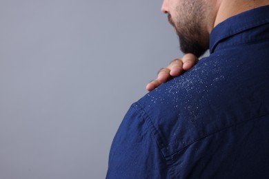 Man brushing dandruff off his shirt on grey background, closeup. Space for text