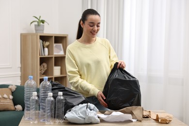 Smiling woman with plastic bag separating garbage in room