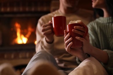 Photo of Lovely couple with delicious cocoa near burning fireplace at home, closeup. Winter vacation