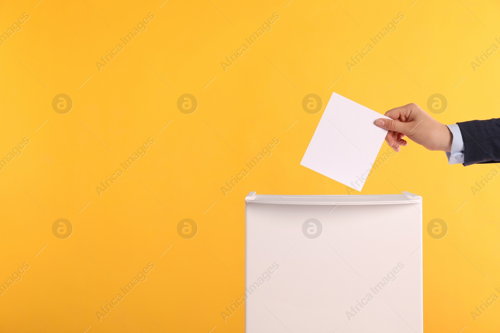 Photo of Woman putting her vote into ballot box on orange background, closeup. Space for text
