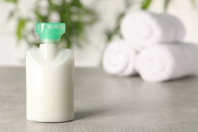 Mini bottle of cosmetic product on light grey table against blurred background, closeup. Space for text