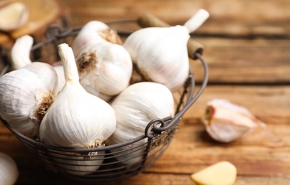 Photo of Fresh organic garlic in basket on wooden table, closeup