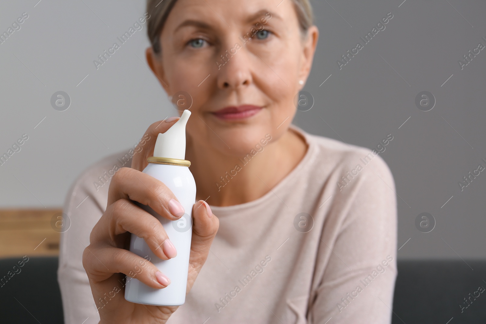 Photo of Woman holding nasal spray indoors, focus on bottle