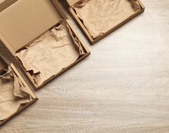 Photo of Open cardboard boxes with crumpled paper on wooden background, flat lay. Space for text