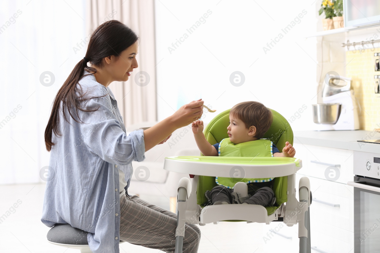 Photo of Young nanny feeding cute little baby in kitchen