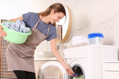Photo of Woman putting laundry detergent capsule into washing machine indoors