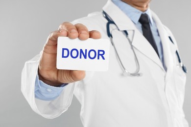 Doctor holding card with word DONOR on light grey background, closeup