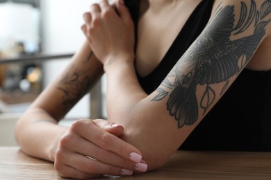 Photo of Beautiful woman with tattoos on arms at table indoors, closeup