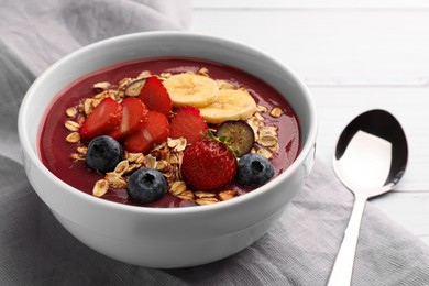 Photo of Delicious smoothie bowl with fresh berries, banana and granola on white wooden table, closeup