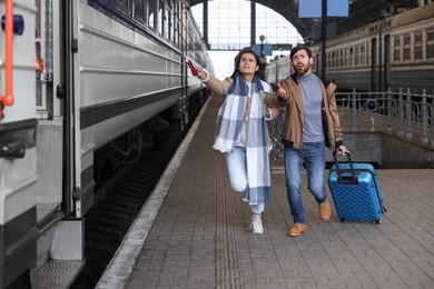 Photo of Being late. Worried couple with suitcase running towards train at station, space for text