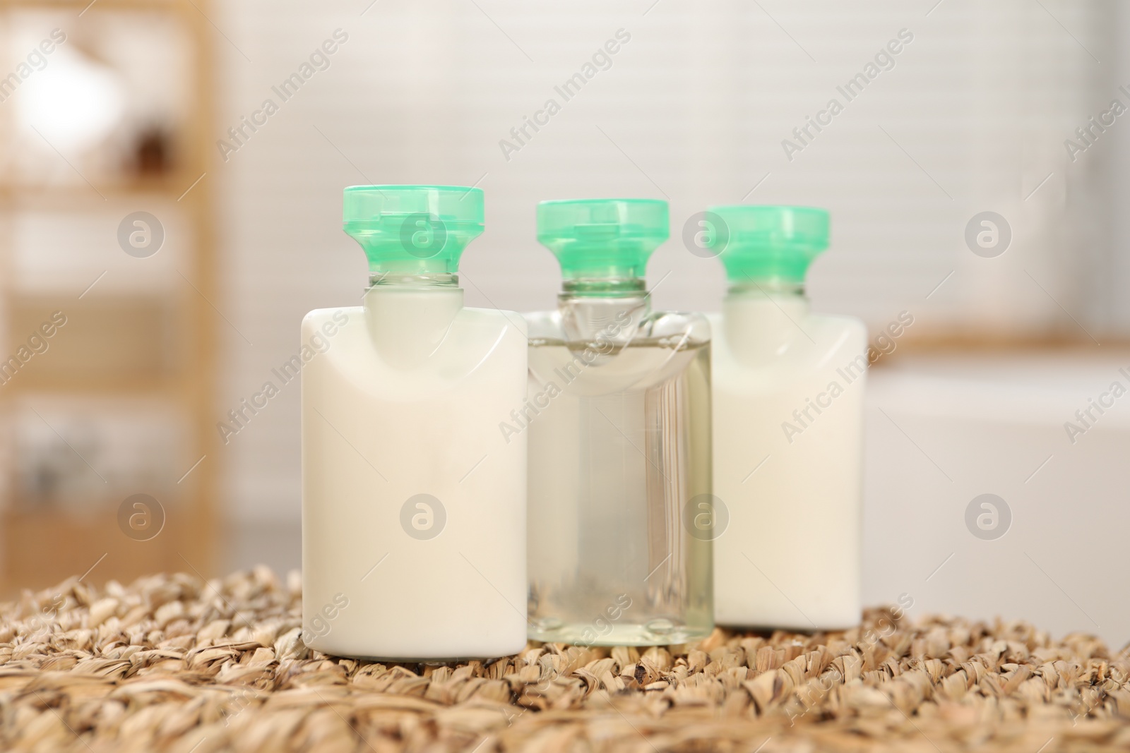 Photo of Mini bottles of cosmetic products on wicker mat against blurred background