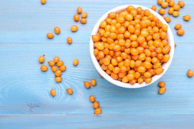 Photo of Bowl with fresh ripe sea buckthorn berries on light blue wooden table, flat lay. Space for text