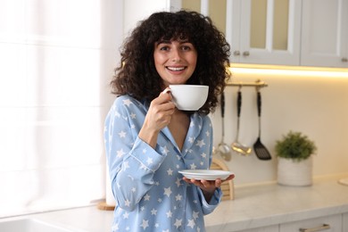 Photo of Beautiful young woman in stylish pyjama with cup of drink in kitchen