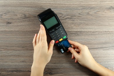 Photo of Woman with credit card using modern payment terminal at wooden table, top view