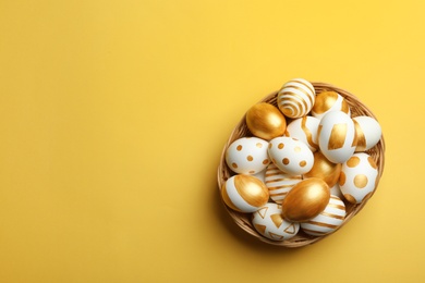 Photo of Wicker basket of traditional Easter eggs decorated with golden paint on color background, top view. Space for text