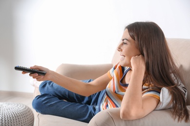 Photo of Beautiful young woman watching TV on sofa at home