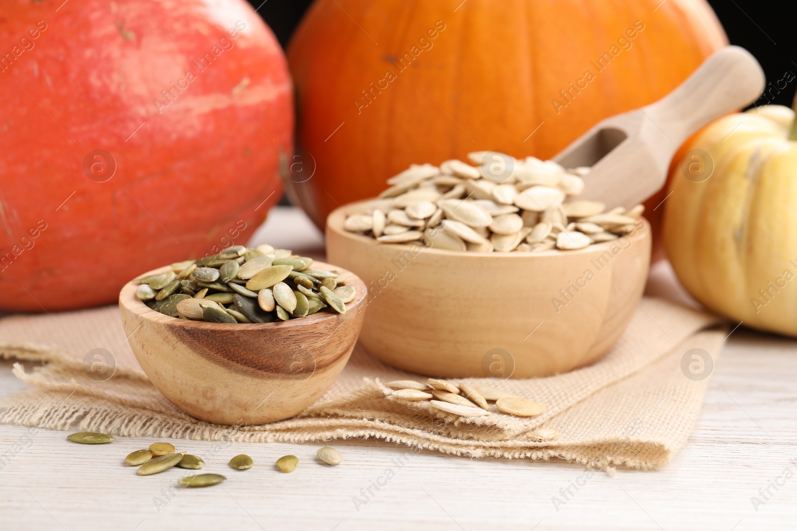 Photo of Bowls with seeds and fresh pumpkins on light wooden table