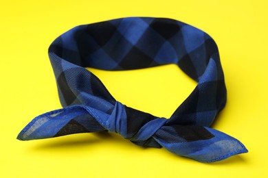 Tied blue checkered bandana on yellow background, closeup