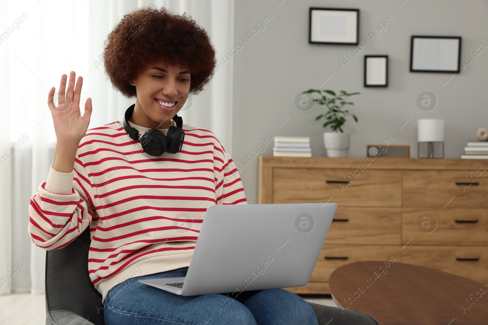 Photo of Beautiful young woman having video chat via laptop and saying hello in room, space for text