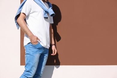 Young hipster man in stylish jeans posing near color wall