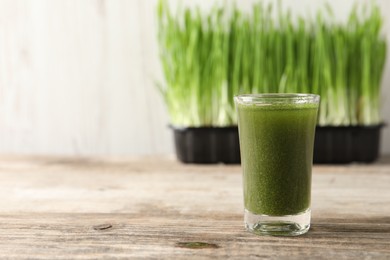 Photo of Wheat grass drink in shot glass on wooden table, closeup. Space for text