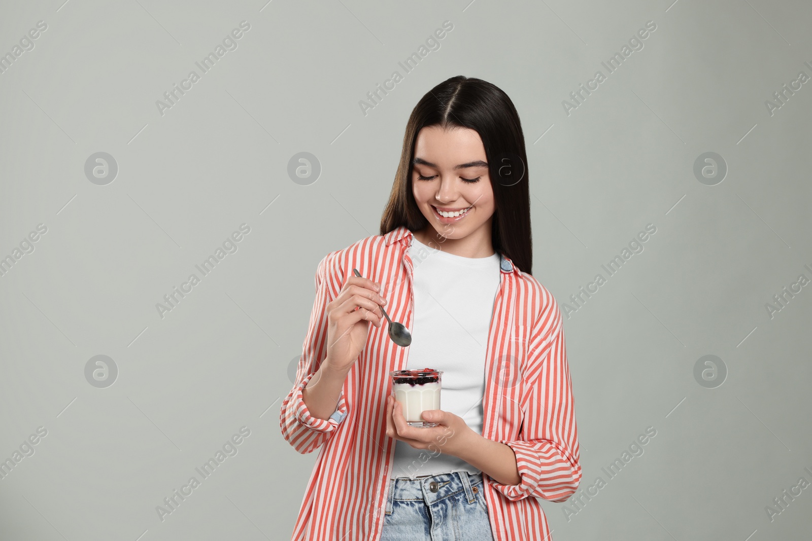 Photo of Happy teenage girl with delicious yogurt and spoon on light grey background. Space for text