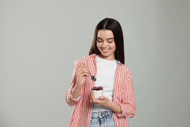 Photo of Happy teenage girl with delicious yogurt and spoon on light grey background. Space for text