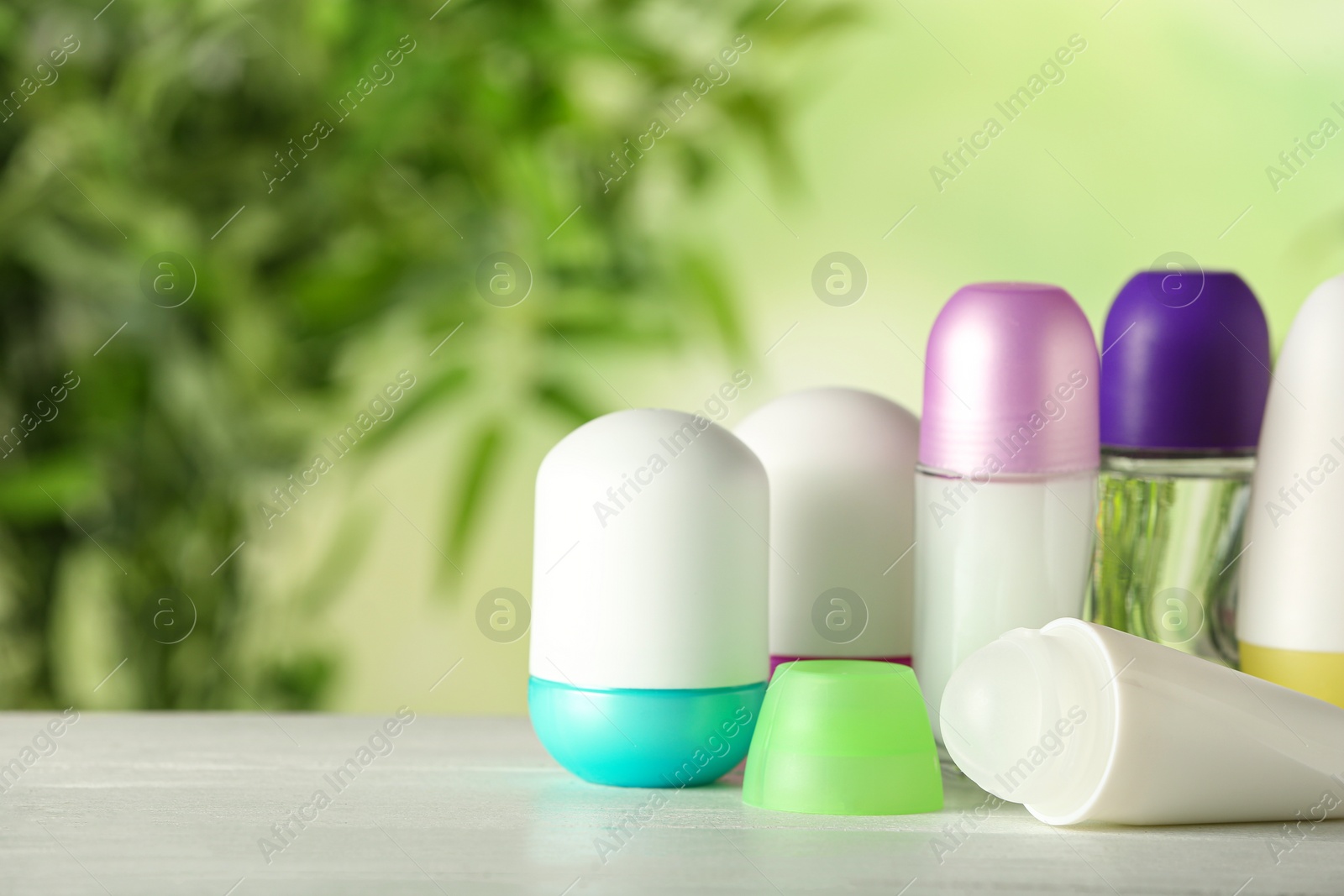 Photo of Different deodorants on white wooden table against blurred background. Space for text