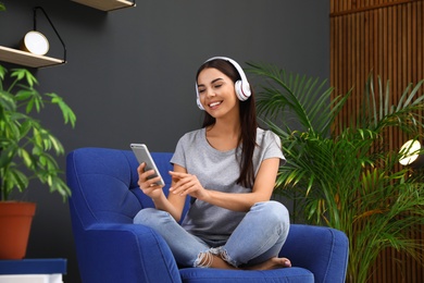 Photo of Happy woman listening to music in armchair at home. Indoor plants for trendy interior design