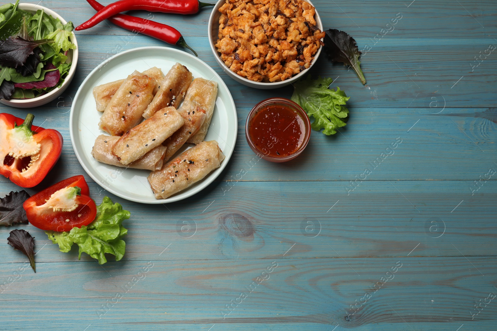 Photo of Tasty fried spring rolls and ingredients on light blue wooden table, flat lay. Space for text