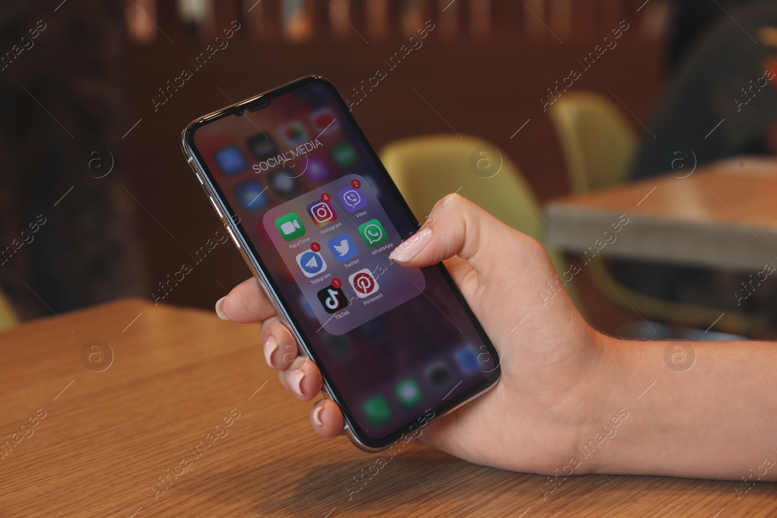 Photo of MYKOLAIV, UKRAINE - AUGUST 11, 2021: Woman using Apple iPhone X at wooden table, closeup. Screen with different social media icons