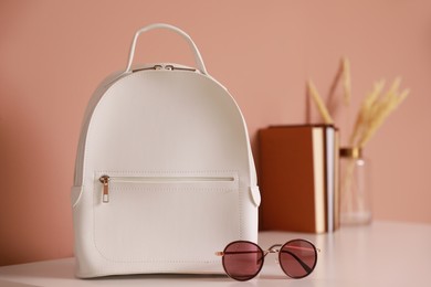 Photo of Stylish white backpack and sunglasses on table indoors