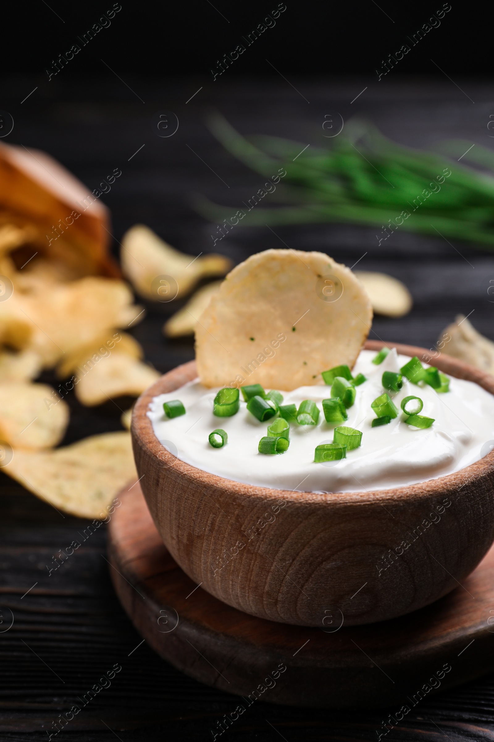 Photo of Sour cream and chips on black wooden table, closeup