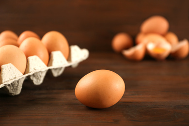 Photo of Raw chicken egg near carton tray on wooden table