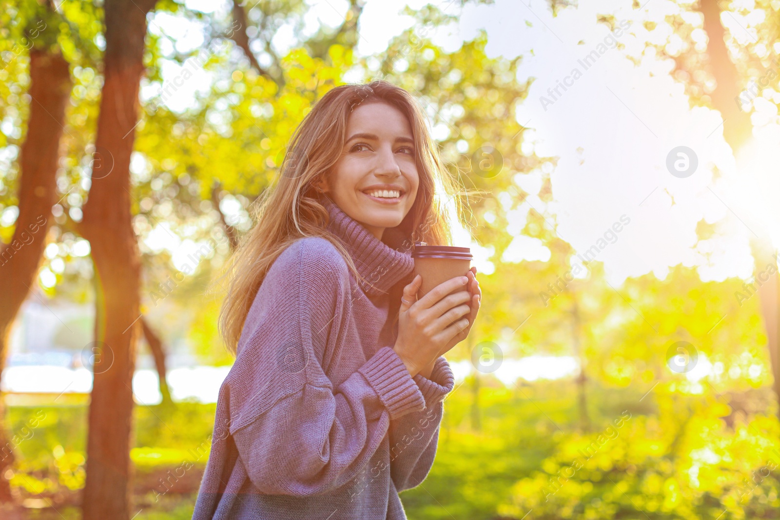 Photo of Beautiful young woman with coffee cup wearing stylish sweater in autumn park