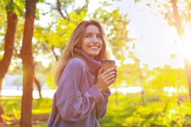 Beautiful young woman with coffee cup wearing stylish sweater in autumn park