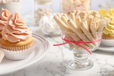 Vase with cookies and tasty cupcakes on white marble table, closeup. Candy bar