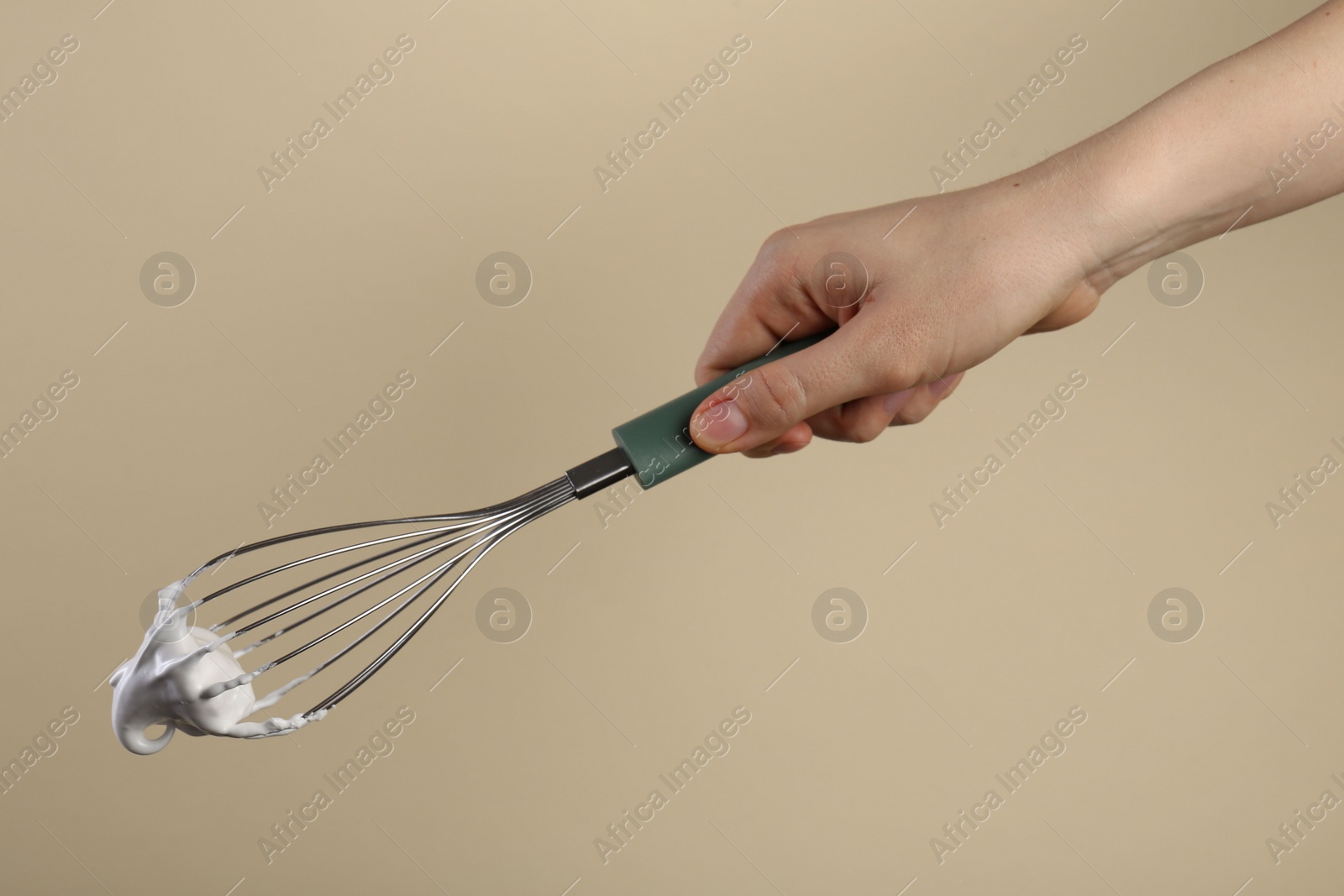 Photo of Woman holding whisk with whipped cream on beige background, closeup