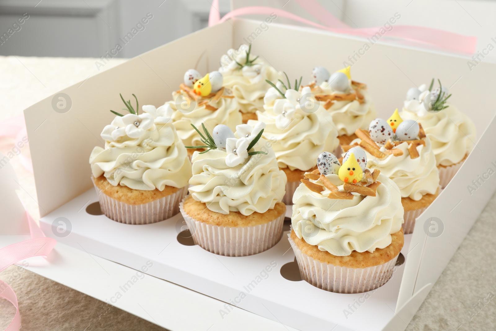 Photo of Tasty Easter cupcakes with vanilla cream in box on table, closeup