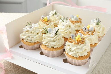 Photo of Tasty Easter cupcakes with vanilla cream in box on table, closeup